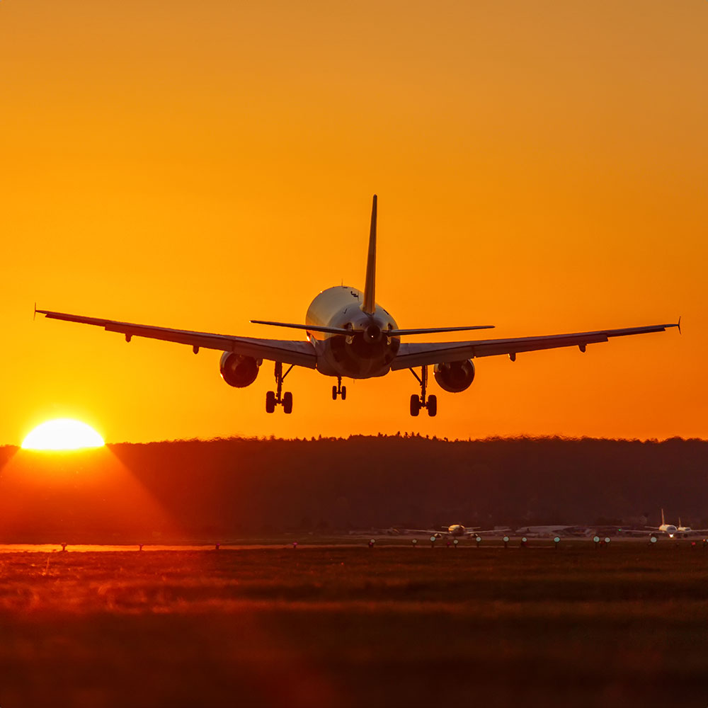 An commercial airliner taking off into an orange sky as the sun is setting